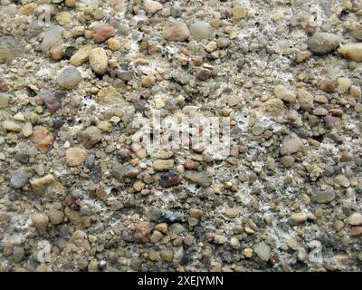 Consistenza di piccoli ciottoli marini. Sfondo senza cuciture in pietra naturale. Superficie ruvida di ciottoli. Vista dall'alto, luce soffusa. Foto Stock