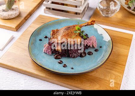 Cosce d'anatra arrosto servite su un piatto blu con cavolo rosso e salsa decorata Foto Stock