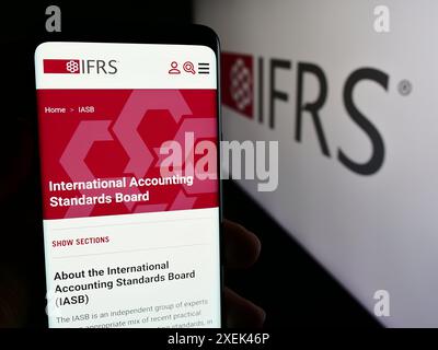 Persona che detiene un cellulare con pagina web dell’International Financial Reporting Standards Foundation (IFRS). Messa a fuoco al centro del display del telefono. Foto Stock