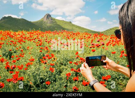 Giovane donna caucasica scatta una foto con il telefono cellulare splendide montagne fiorite fiori all'aperto a Marneuli Georgia, Caucaso. Flusso papavero Foto Stock