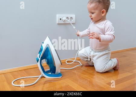 Un bambino e un ferro da stiro collegati a una presa. Concetto di pericolo in casa per un bambino Foto Stock