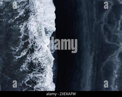 Veduta aerea della spiaggia di sabbia nera con onde bianche e spumose in Islanda Foto Stock