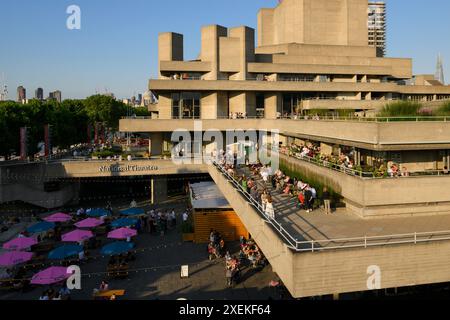 Persone sedute sulle terrazze del Teatro Nazionale godendosi il sole della sera. Il National Theatre fa parte del Southbank Centre. Il teatro Foto Stock