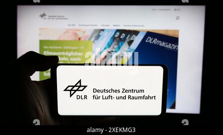 Persona che detiene un cellulare con il logo di Deutsches Zentrum für Luft- und Raumfahrt e.V. (DLR) davanti alla pagina web. Mettere a fuoco il display del telefono. Foto Stock