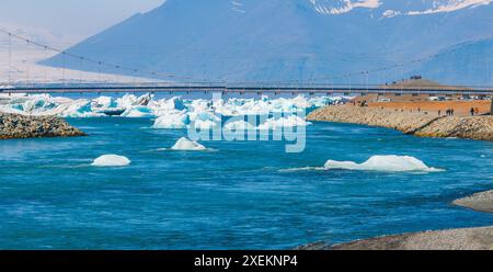 Ponte sospeso sul fiume ghiacciato con montagne innevate in Islanda Foto Stock