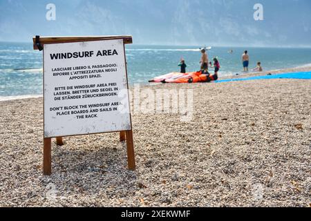 Torbole, Lago di Garda, Italia - 27 giugno 2024: Cartello con l'iscrizione area Windsurf, area segnaletica a Torbole di windsurf e sport acquatici, che si trova sulla spiaggia accanto ad una spiaggia balneare. L'accesso con una tavola da surf e una vela da windsurf è più facile qui. *** Schild mit Aufschrift Windsurf area, signalisiert Bereich a Torbole von Windsurfen und Wasserport, welche am Strand neben einem Badestrand liegt. Der Einstieg mit dem Surfbrett und Windsurfsegel ist hier einfacher. Foto Stock