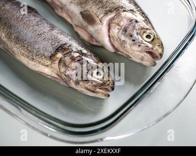 Due salmoni interi freschi in una teglia da forno in vetro, preparazione del cibo, pesce arrosto, cibo per la prestata Foto Stock