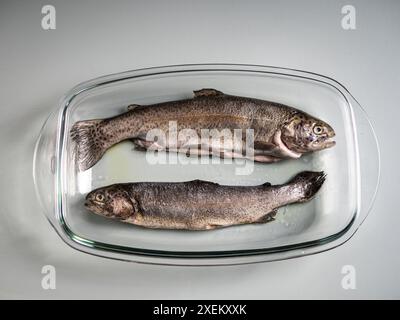 Due salmoni interi freschi in una teglia da forno in vetro, preparazione del cibo, pesce arrosto, cibo per la prestata Foto Stock