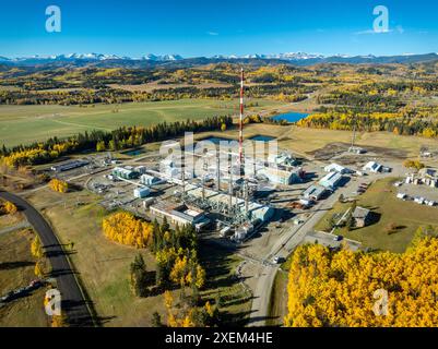 Vista aerea dell'impianto a gas con alberi autunnali dai colori vivaci, colline, montagne e cielo blu sullo sfondo, a sud-ovest di Bragg Creek in Alberta Foto Stock