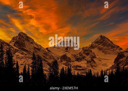 Spettacolare formazione di nuvole colorate sopra una catena montuosa innevata e alberi sempreverdi sagomati in primo piano, a sud di Canmore, Alberta Foto Stock