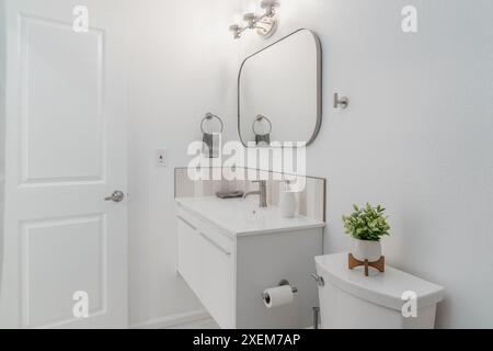 bagno moderno di colore bianco con mobile galleggiante, lavandino, rubinetto, specchio, luci, e toilette con dettagli grigi Foto Stock