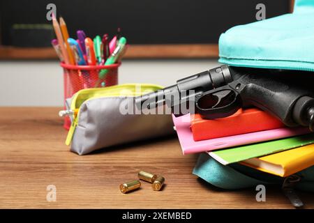 Pistola, proiettili e cancelleria scolastica su un tavolo di legno vicino alla lavagna interna, primo piano Foto Stock