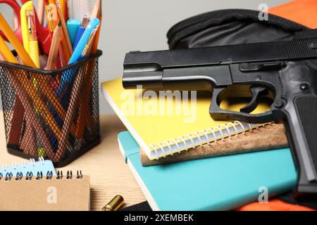 Pistola, proiettili e cancelleria scolastica su un tavolo di legno, primo piano Foto Stock