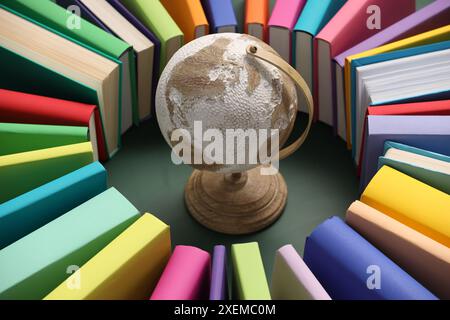 Globo circondato da molti libri colorati su sfondo verde, primo piano Foto Stock
