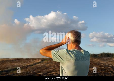 Primo piano di un uomo che è sulla schiena e ha le mani sulla testa che guarda il suo campo bruciato dopo l'incendio. Sullo sfondo dell'immagine è presente del fumo. Foto Stock