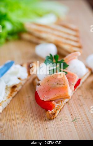 toast fritti con salmone, formaggio spalmabile, insalata, su un tavolo di legno. Foto Stock