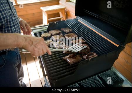 L'uomo anziano cucina hamburger su una griglia.; Elkhorn, Nebraska, Stati Uniti d'America Foto Stock