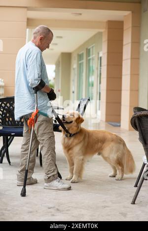 L'uomo paraplegico con stampelle all'avambraccio fa un segno di mano e riceve assistenza da un cane di servizio addestrato; Boynton Beach, Florida, Stati Uniti d'America Foto Stock