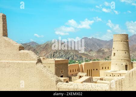 Fortezza della cittadella di Bahla mura in pietra e torri rotonde con montagne sullo sfondo, Bahla, Oman Foto Stock