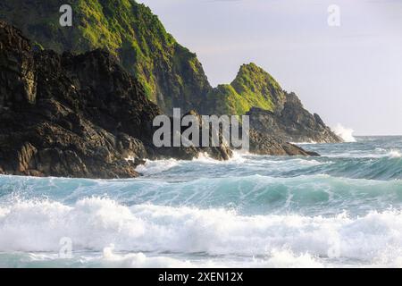 Terreni accidentati ricoperti di vegetazione verde e che si schiantano per il surf lungo un'isola indonesiana a Telawas Beach Foto Stock