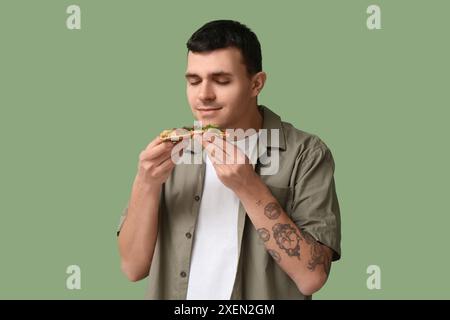 Giovane con un pezzo di gustosa pizza su sfondo verde Foto Stock