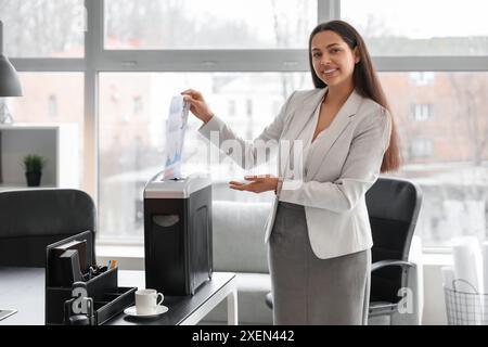 Giovane segretaria che distrugge i documenti usando il tritadocumenti in ufficio Foto Stock