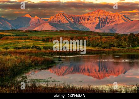 Splendida vista della catena montuosa che si riflette nel piccolo lago all'alba con una calda luce rossa dorata, che illumina il versante della montagna, le colline ondulate e la piscina... Foto Stock