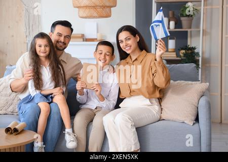 Felice famiglia ebraica con libro e bandiera di Israele seduti sul divano di casa Foto Stock