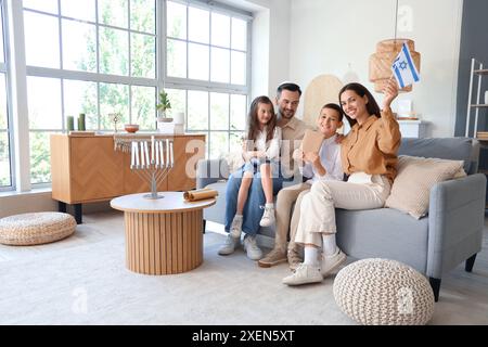 Felice famiglia ebraica con libro e bandiera di Israele seduti sul divano di casa Foto Stock