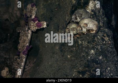 Teschi umani e croce decorativa ricoperta di fiori nell'antico cimitero di Londa all'interno di Sulawesi Selatan, Indonesia Foto Stock