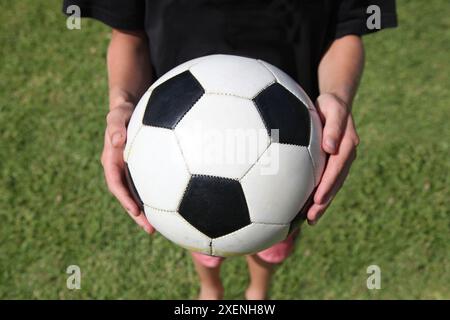 Un ragazzo tiene una palla da calcio sopra l'erba verde Foto Stock