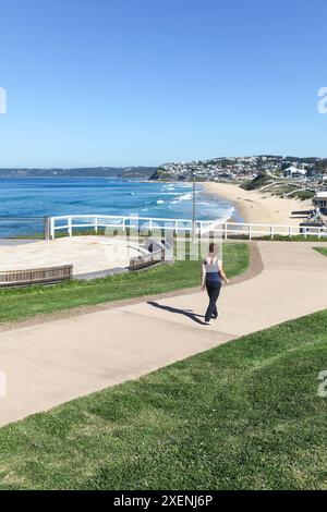 Una donna cammina lungo la passerella costiera di recente costruzione a Bar Beach - Newcastle Australia e una bella giornata d'autunno soleggiata. Foto Stock