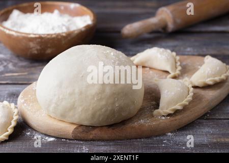 Impasto per gnocchi su un tagliere di legno, gnocchi pronti, una ciotola di farina e un mattarello per stendere l'impasto su un tavolo di legno Foto Stock