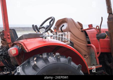 Primo piano di un vecchio trattore rosso con pneumatici usurati e parti arrugginite. Foto Stock