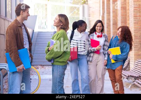 Gruppo multietnico di studenti che camminano con i quaderni, ridono. Foto Stock