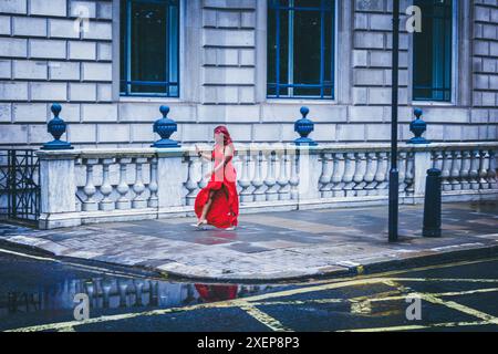 Una donna con un vestito rosso cammina con il suo cellulare in mano, ottenendo indicazioni per la sua destinazione Foto Stock