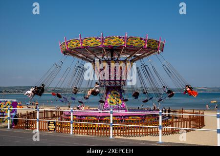 Fai un giro in giostra sulla spiaggia di Weymouth in una giornata estiva con un cielo azzurro Foto Stock