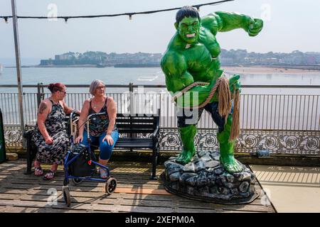Due donne che riposano su una panchina accanto ad un modello dell'incredibile Hulk, Paignton Pier, Devon Foto Stock