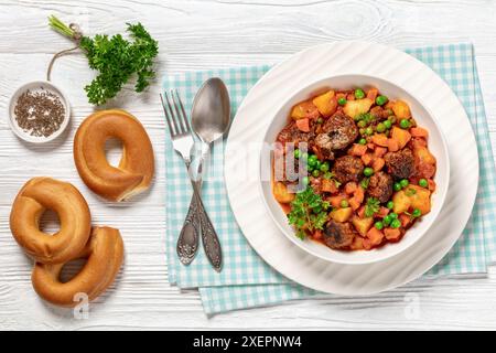 stufato turco di polpette, sulu kofte, piatto abbondante con patate, carote e piselli verdi sospesi in salsa di pomodoro servito in un recipiente con forchetta e cucchiaio su w. Foto Stock