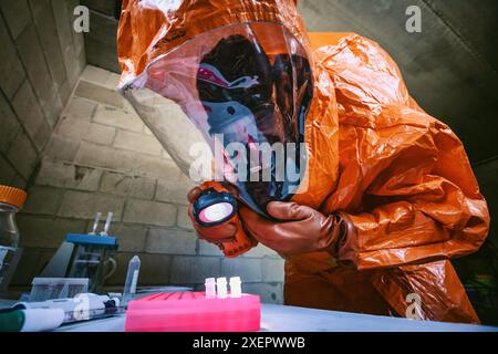 Un uomo che indossa una tuta protettiva completa in un laboratorio con sostanza biologica infettiva in provette - indagine sulla scena del crimine Foto Stock