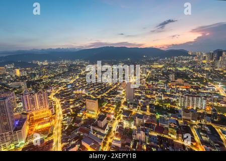 Vista sul tetto dell'area del centro città al tramonto, con sentieri leggeri dal traffico e dopo il bagliore di sole dietro colline lontane, dalla piattaforma dell'osservatorio di George Town Foto Stock