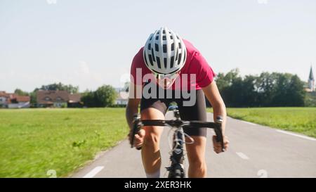 Giovane donna professionista bicyclist durante la corsa su strada, movimento continuo con massimo sforzo, vista ravvicinata. Foto Stock