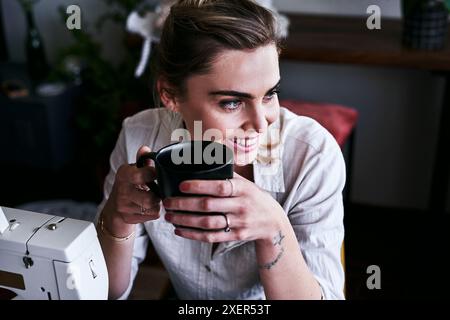 Donna di moda, boutique e business che pensa con un caffè in ufficio per cucire, creare o personalizzare la macchina. Abbigliamento, fabbrica o designer con Foto Stock