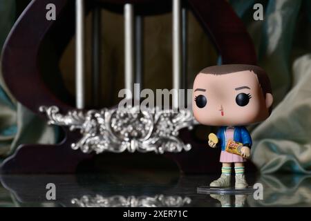 Action figure Funko Pop in vinile di Eleven with Eggo waffles della popolare serie TV Stranger Things. Pavimento riflettente, tenda verde, palazzo d'epoca. Foto Stock