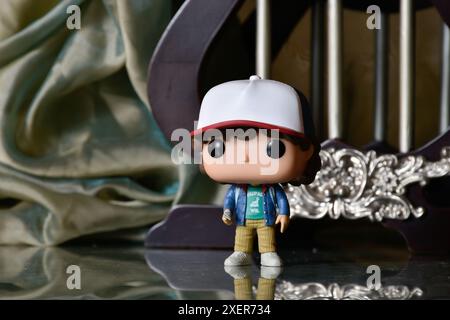 Funko Pop action figure di Dustin Henderson della popolare serie TV di Netflix Stranger Things. Pavimento riflettente, tenda verde, gabbia vintage, colonne. Foto Stock