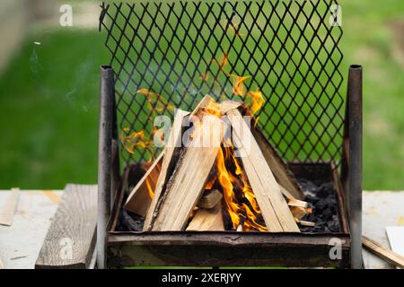 il fuoco è stato avviato con tronchi di legno su una griglia all'aperto che si prepara per un barbecue. giardino. bruciate il barbecue Foto Stock