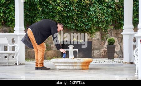 Karlsbad, Cecochia, 10 giugno 2024: Un uomo riempie acqua minerale curativa in una bottiglia blu in una sorgente pubblica a Karlovy Vary Foto Stock