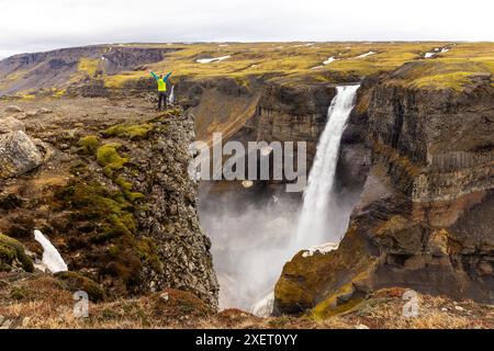 Cascata Haifoss nella valle di Fossardalur in Islanda, vista panoramica del profondo canyon coperto da una viaggiatrice in piedi sulla scogliera. Foto Stock