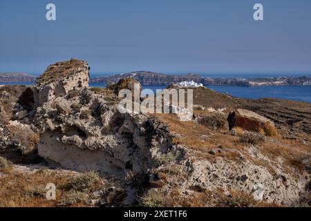 Roccia vulcanica della pomice e il monastero di Moni Kimisi Theotokou sulla punta meridionale di Thirasia, con Santorini in lontananza. Isole Cicladi, Greec Foto Stock