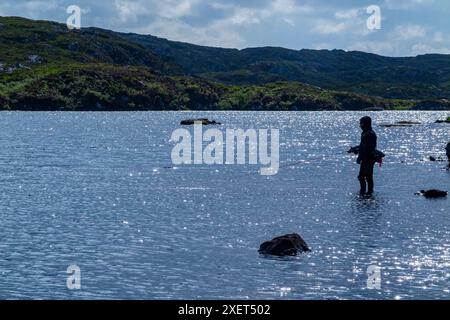Un pescatore di mosca suona un pesce nelle remote colline di Assynt, in Scozia Foto Stock